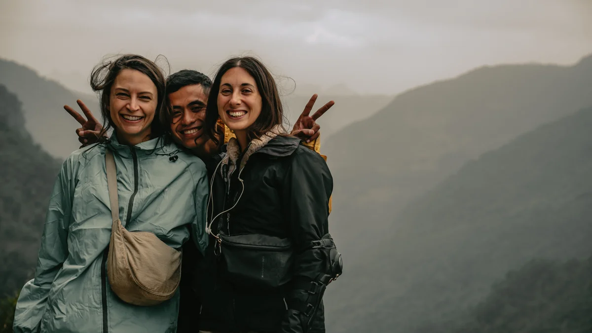 Three people smile and pose for the camera with mountains behind