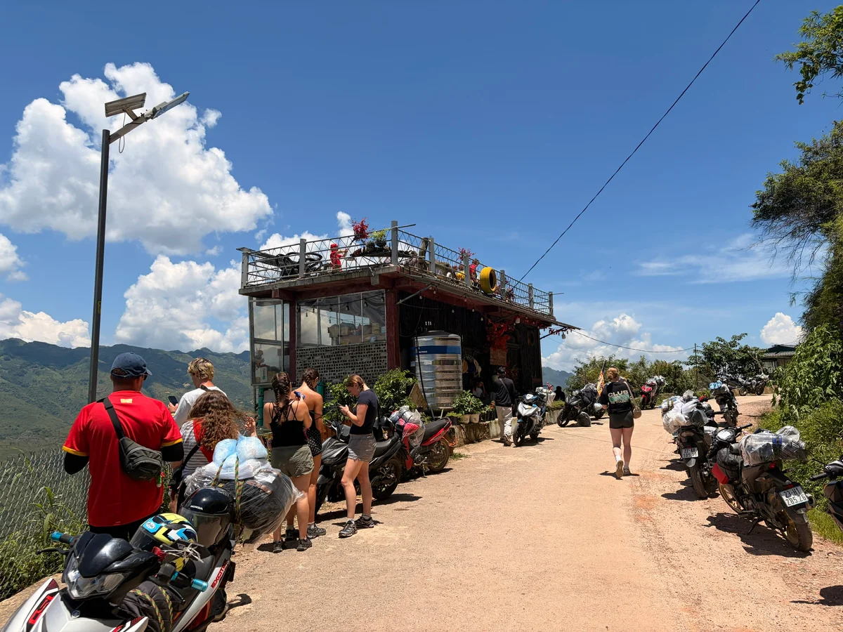 A dirt road with a coffee shop and people and motorbikes around