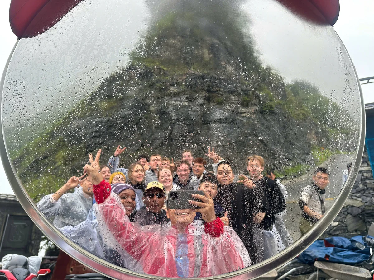 Group of people pose in a traffic mirror with peace signs in rain coats