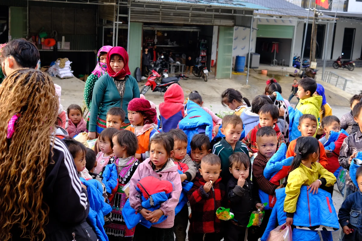 A group of school children in colourful clothing stand together facing the camera