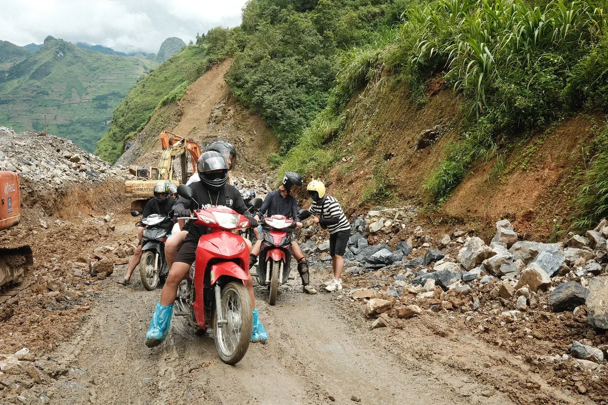 A group of people on motorbikes navigate muddy, dangerous-looking roads