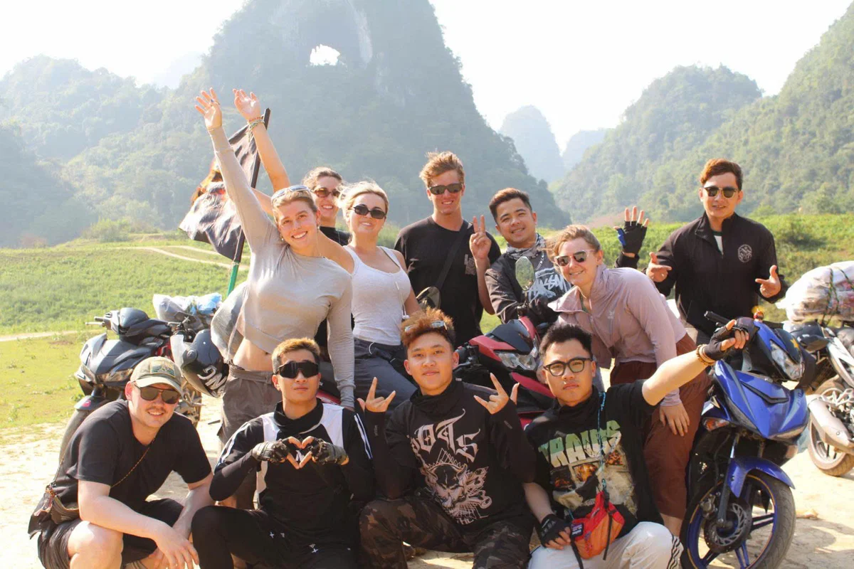 Group of people smile and huddle together putting their arms up with a mountain with a hole in it behind