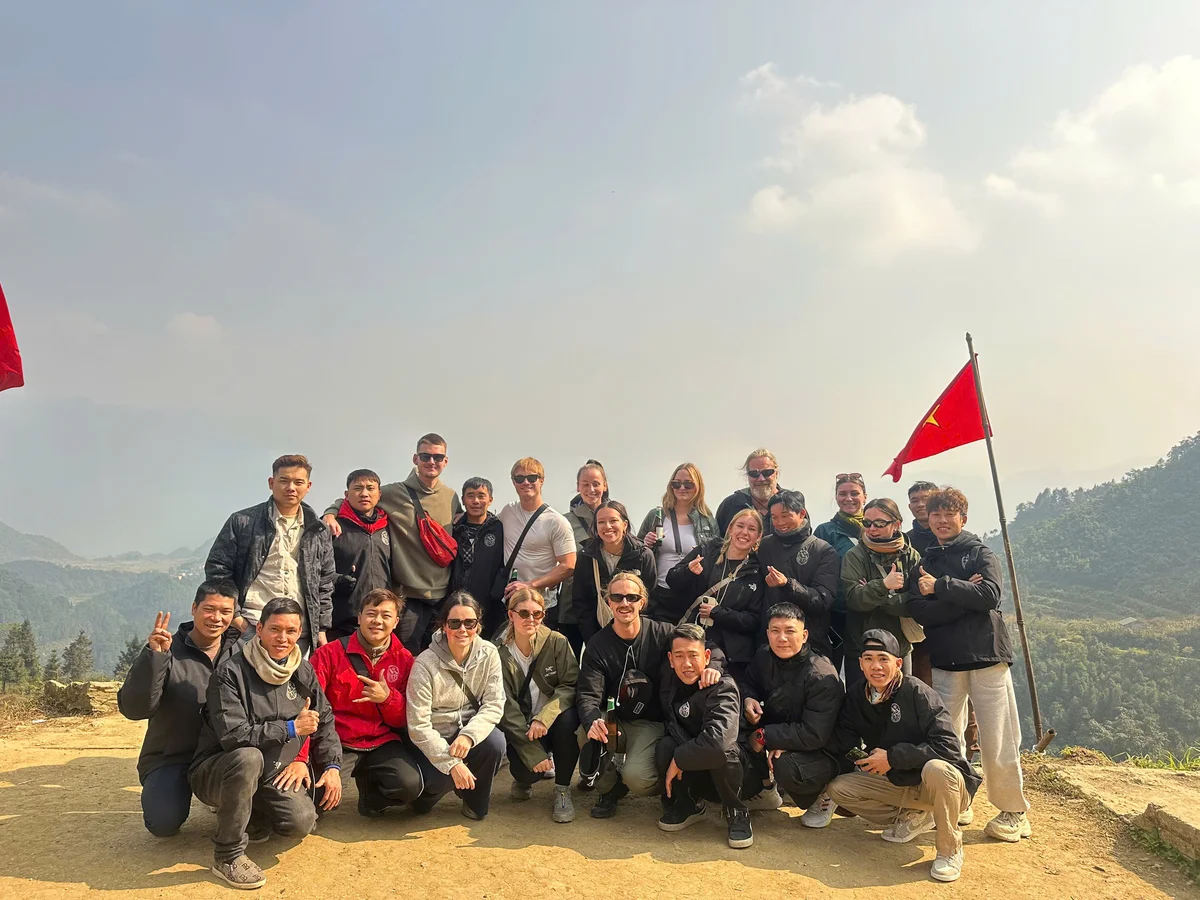 Group of people pose with vietnamese flag and mountains in the background