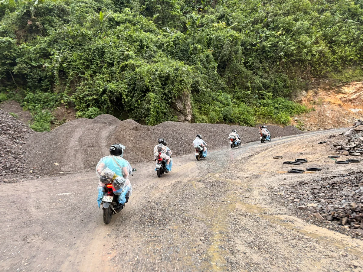 Group of passengers sit behind drivers riding together on motorbikes on wet gravel section
