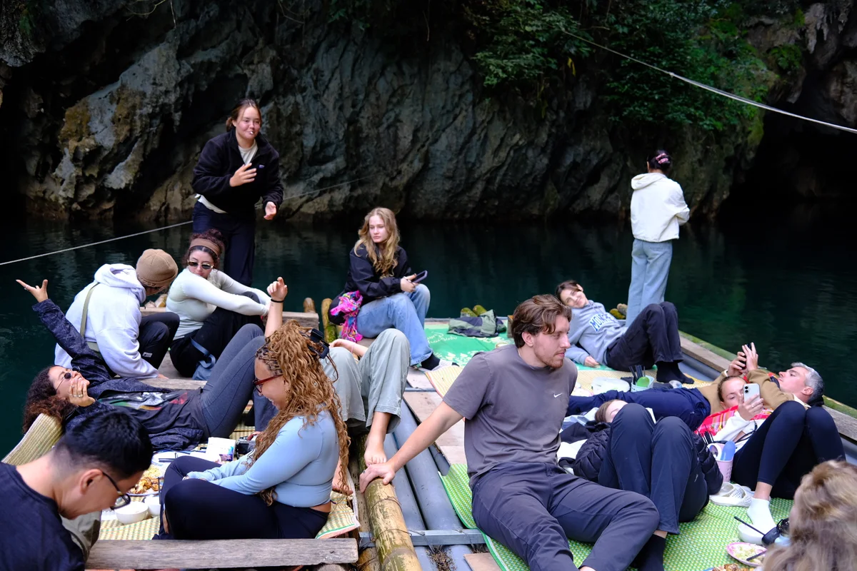 A group of people sit relaxing on a wooden bamboo raft