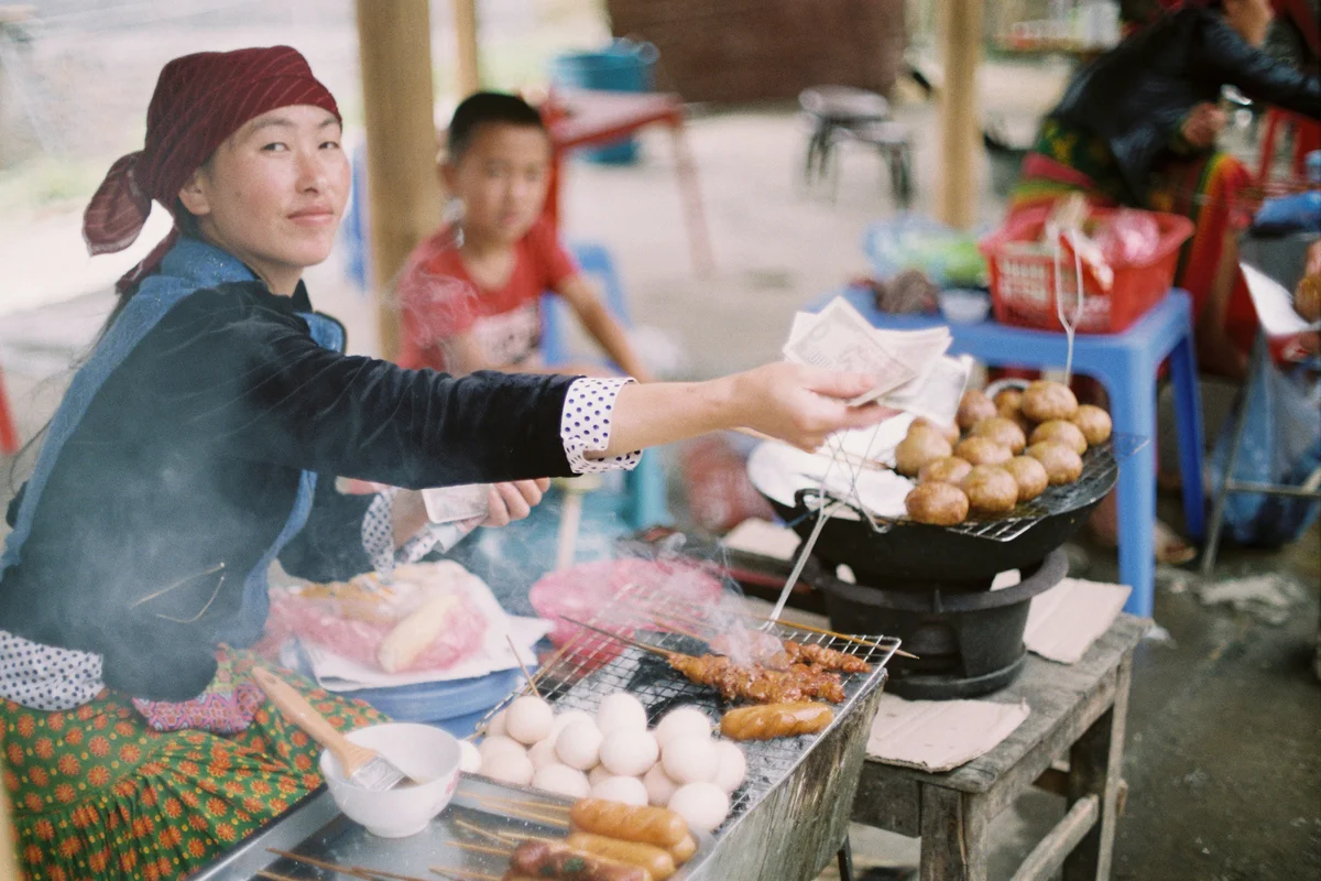 A woman with a head scarf on serves street-food style dishes at a market stall