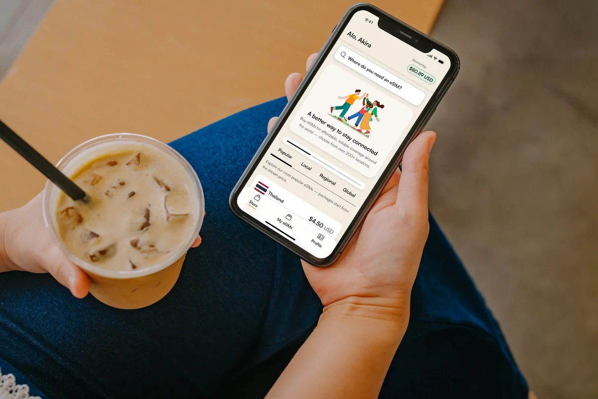 Airalo app open on a person's phone. In the other hand they hold a coffee