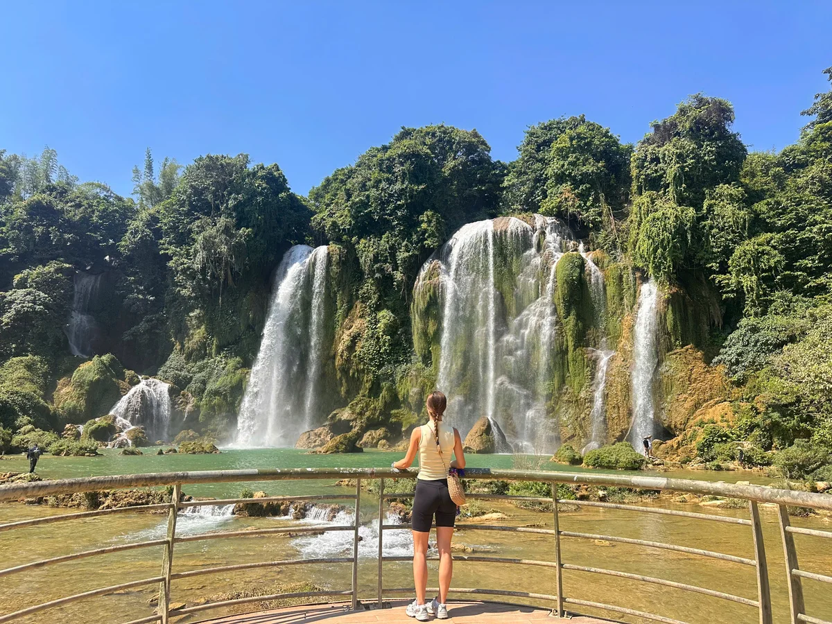 A girl standing at a railing looking out over a huge waterfall