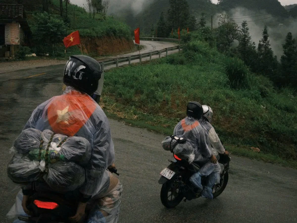 Four people on the back of two separate motorbikes dressed in ponchos on mountains roads.