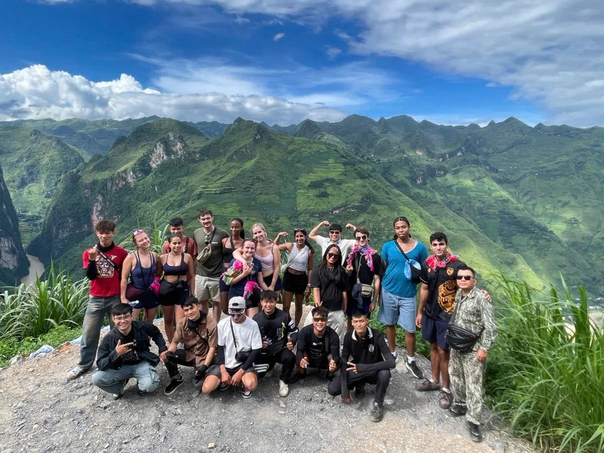 Group of people pose in front of mountains with blue skies and clouds