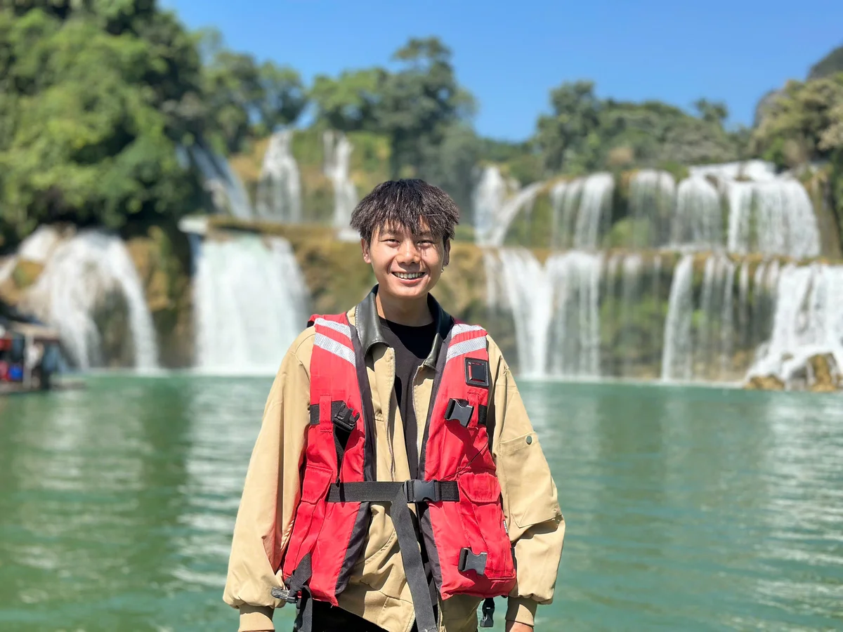 A man stands in front of a huge waterfall and lake