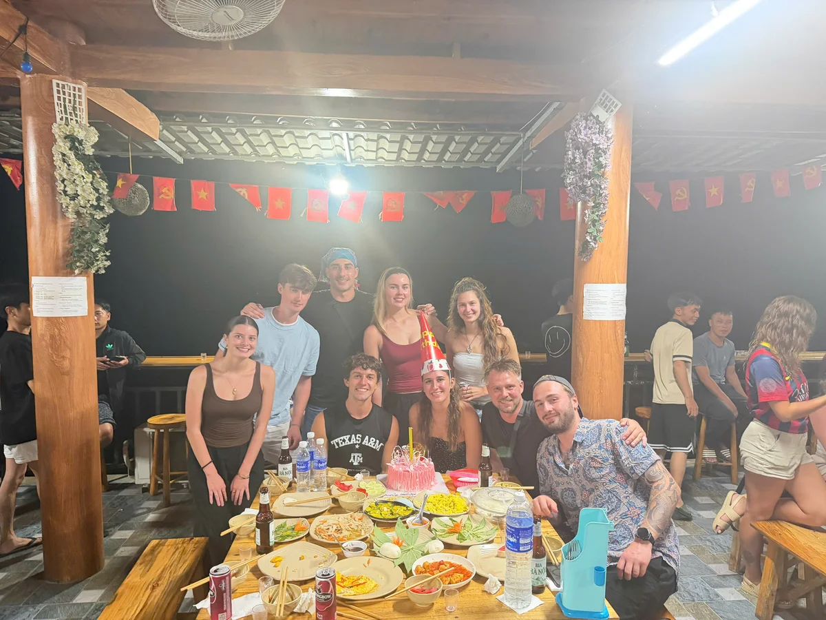 A group of people sit and stand around a table filled with delicious food