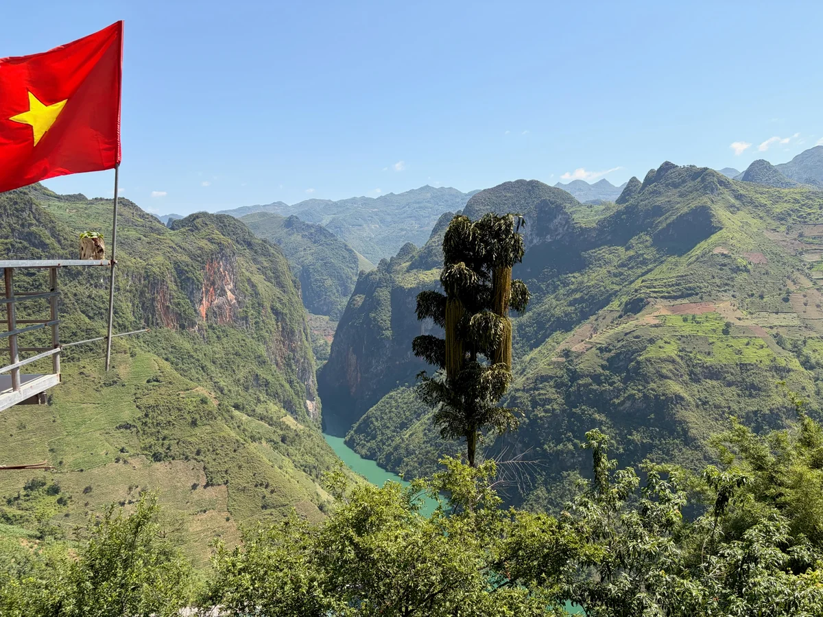 Blue river winds between green mountains and a red flag with a yellow star flaps in the wind