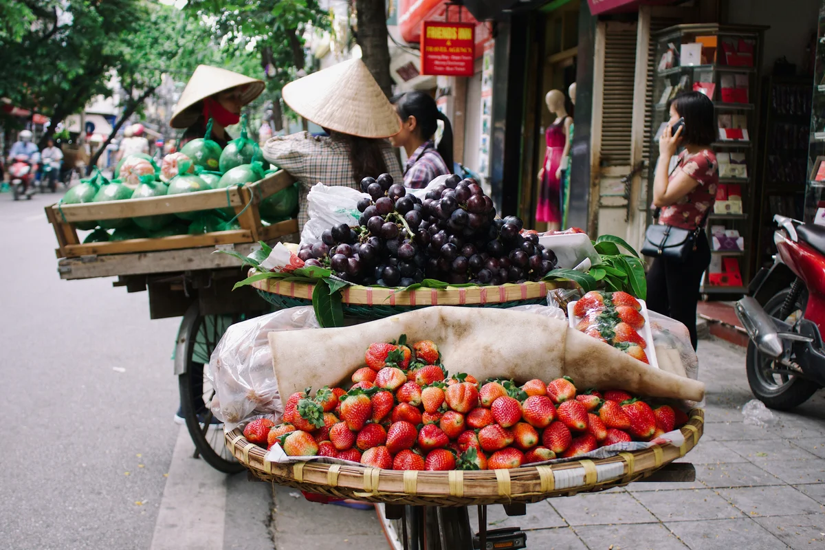 Woman wearing cone hat selling fruit from baskets in the street