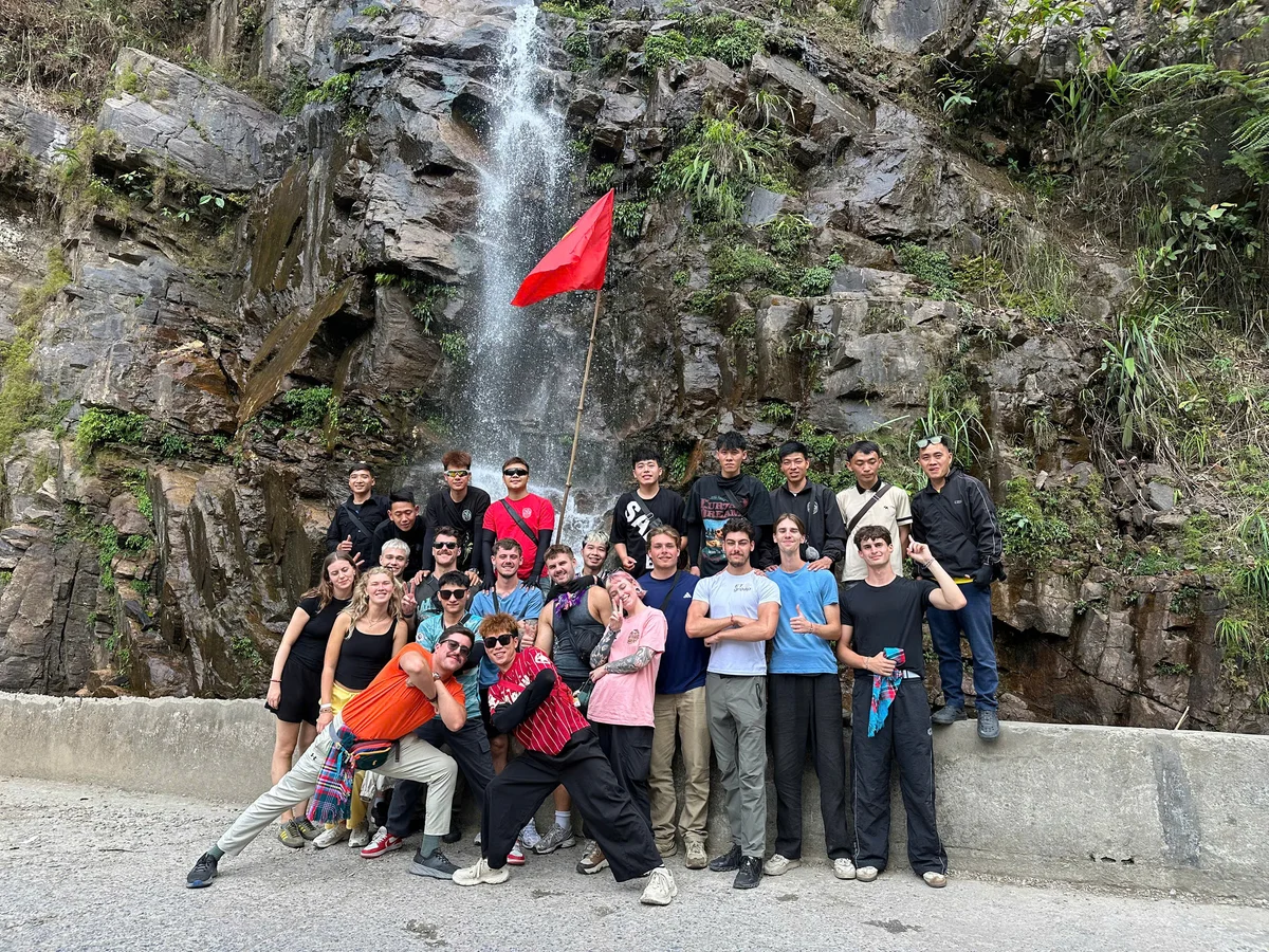 Group of people pose in front of a waterfall streaming down a rock