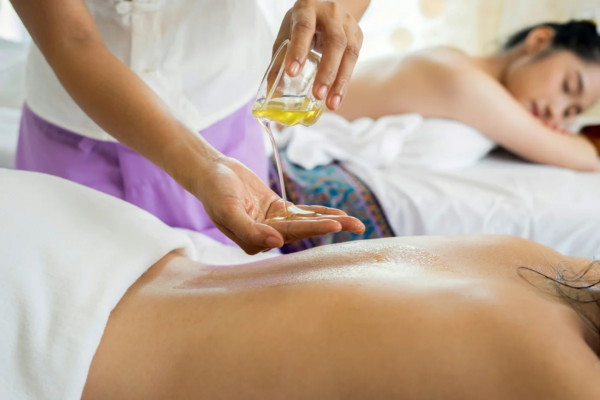 Woman pouring oil into hands as two women lay with their backs exposed on massage tables