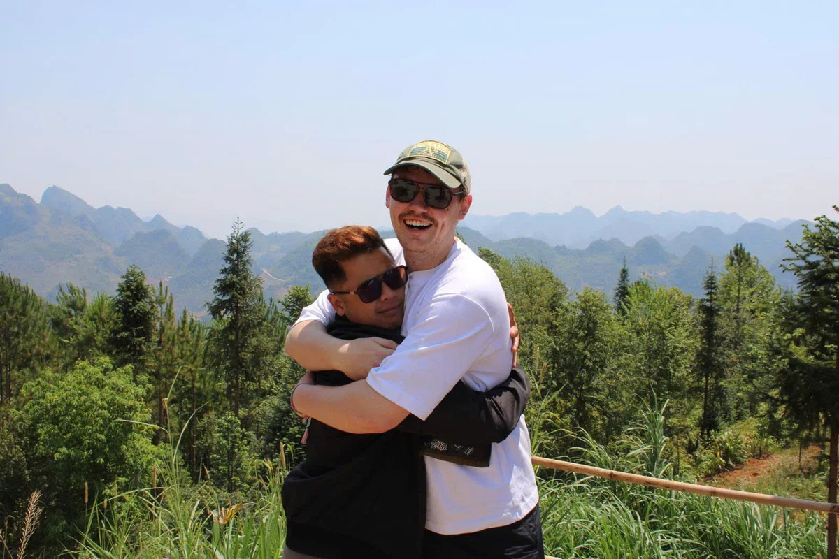 Two men hugging surrounded by forests, mountains and blue skies
