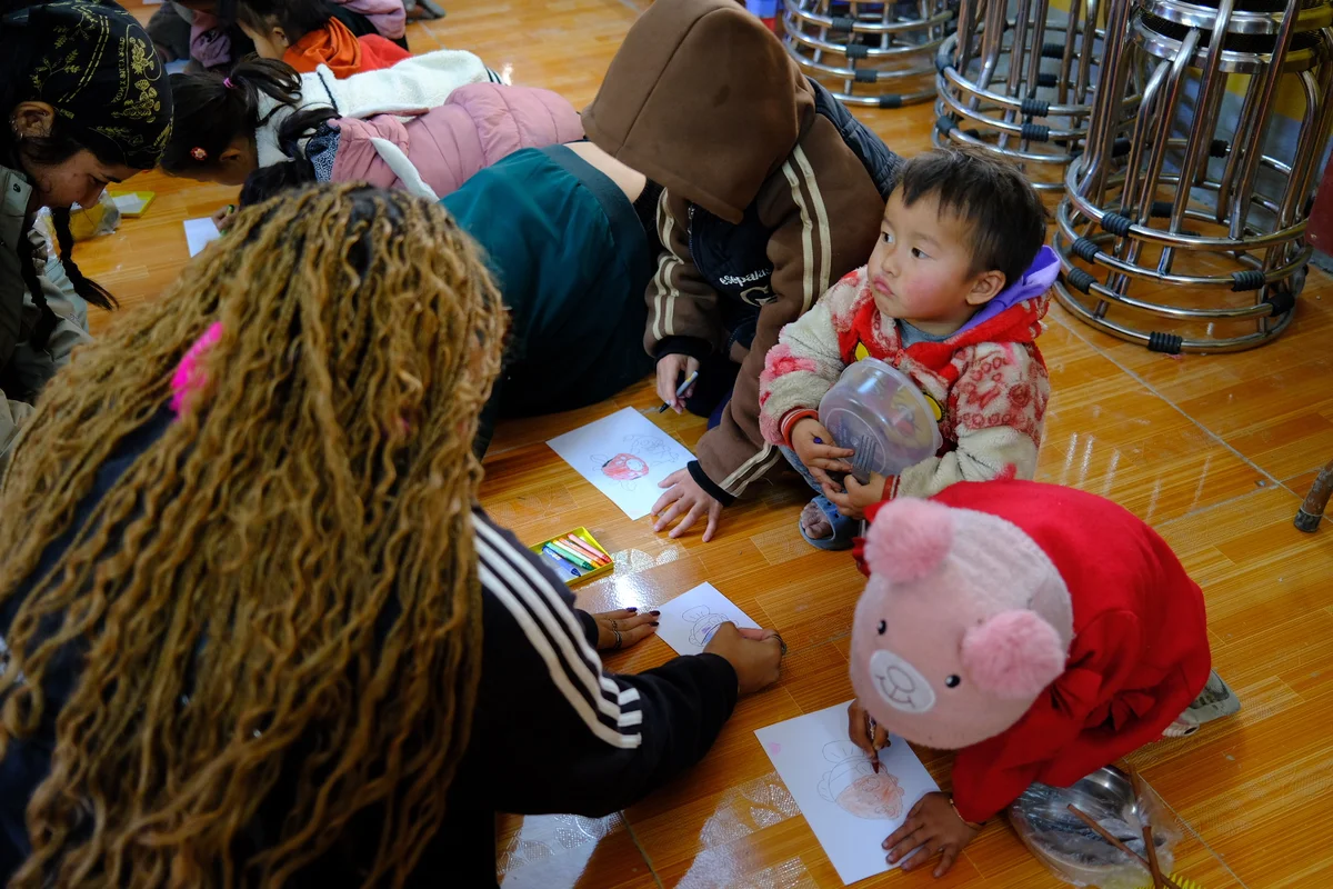 A woman helps some children with some drawing as they all sit on the floor