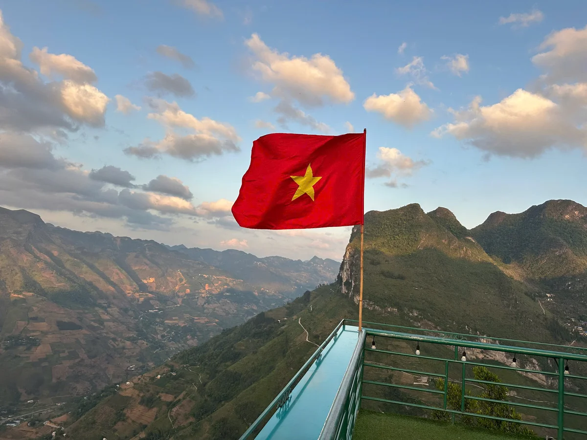 Red flag with a yellow star in the centre furling in the wind with mountains beyond