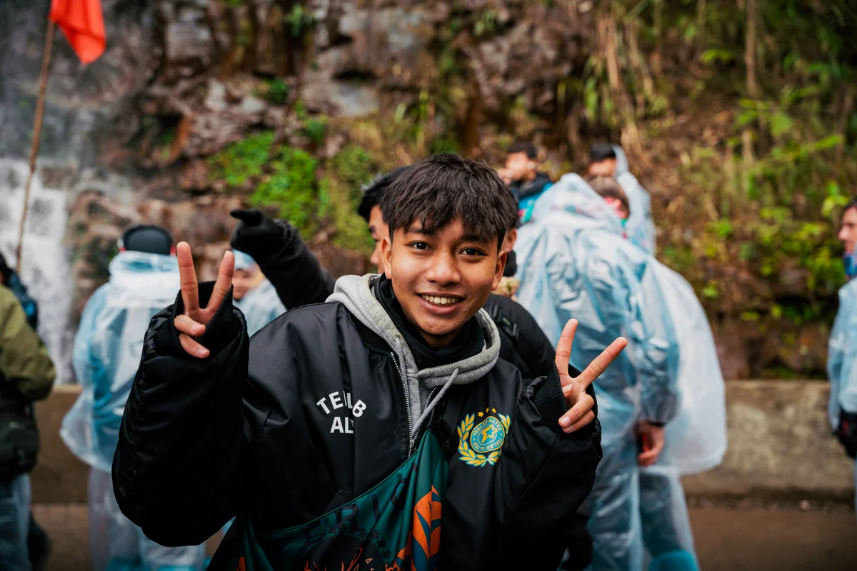 A man makes peace signs for the camera with people wearing ponchos behind