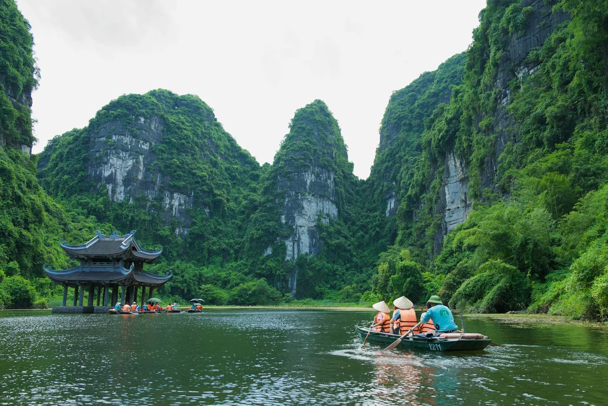 a boat cruises down a peaceful river setting with a temple and big karst mountains behind