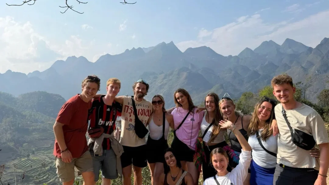 Group of smiling people with arms over each other pose in front of mountains