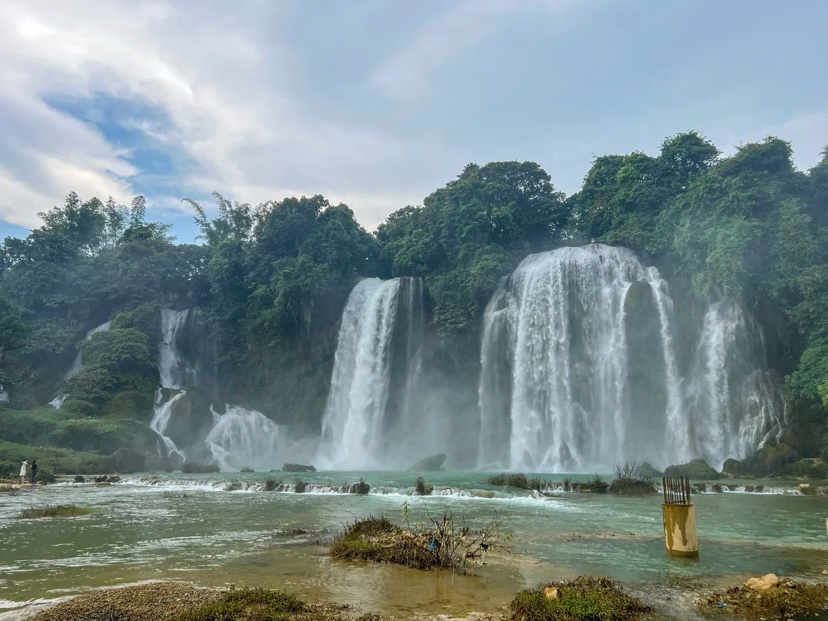 A huge waterfall tumbles down into pools of blue water with trees all around