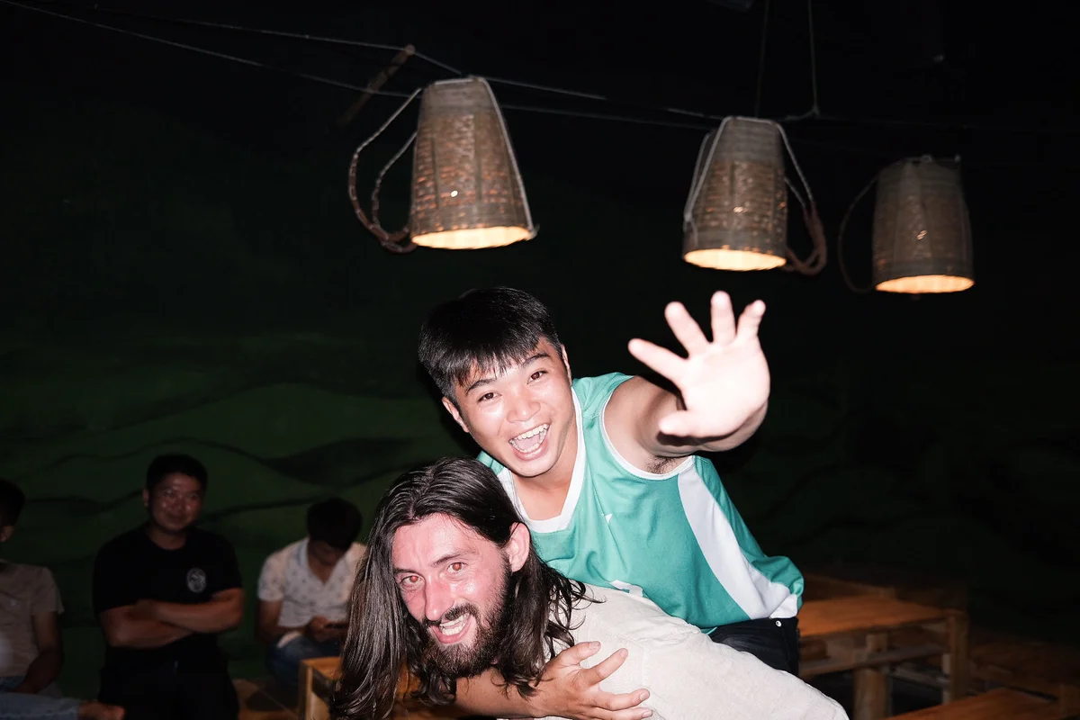 Man is hugging another man, and puts his hand up to the camera. Both men are smiling