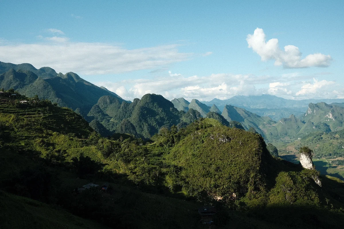 Mountains with lush greenery under a blue sky with clouds. Rolling hills and valleys create a serene and expansive landscape.