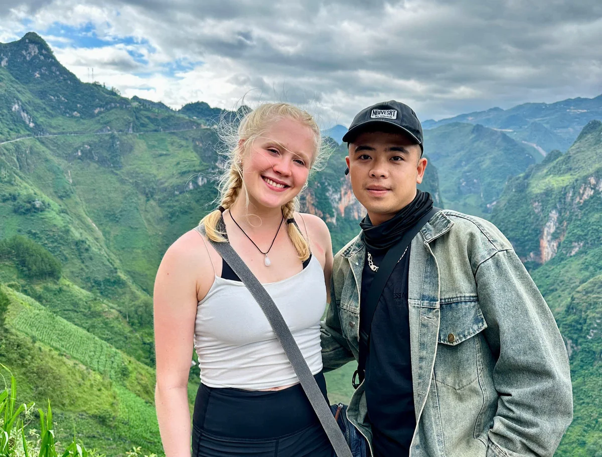 Man and woman pose in front of moody skies and lush green mountains