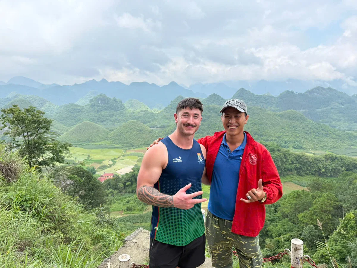 Two men pose infront of green mountains