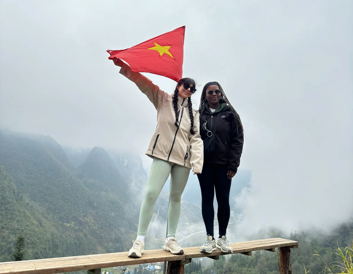 Two new friends on the Ha Giang Loop tour hold a flag against a mountain backdrop.