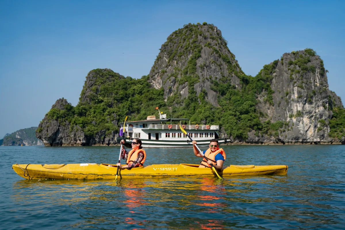 Two people kayaking with a cruise ship and small islands behind