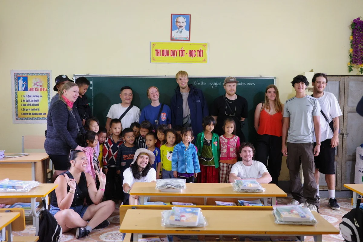 Group of adults and children smiling in a classroom. Chalkboard in background. Sign reads "THI ĐUA DẠY TỐT - HỌC TỐT". Bright, cheerful mood.