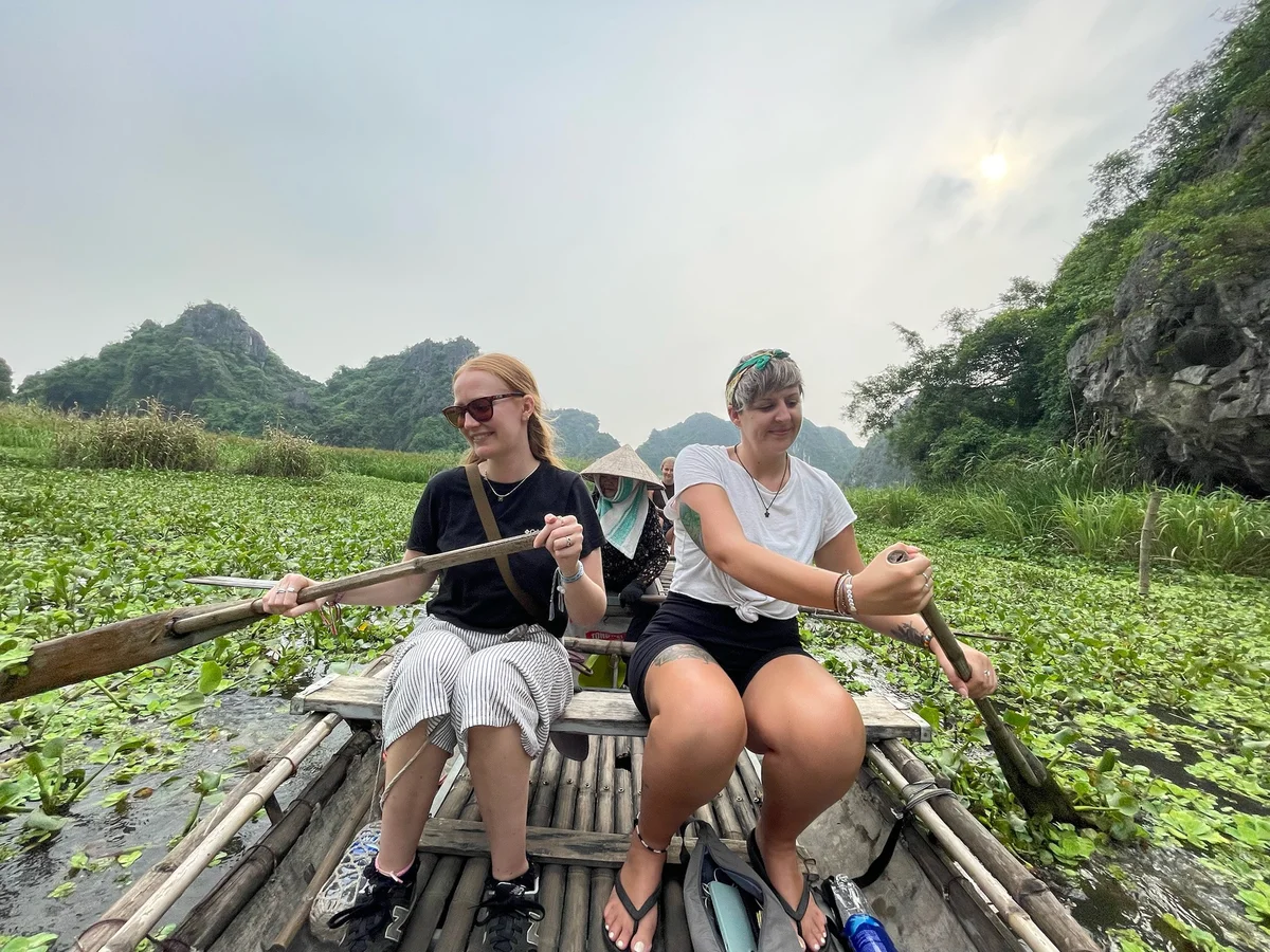 Two women rowing a traditional sampan boat and smiling