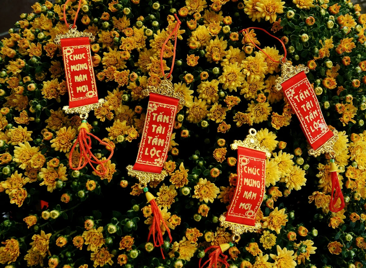 Red Vietnamese New Year banners with gold details hang over vibrant yellow chrysanthemums. Text reads "Chúc Mừng Năm Mới" and "Tấn Tài Tấn Lộc".