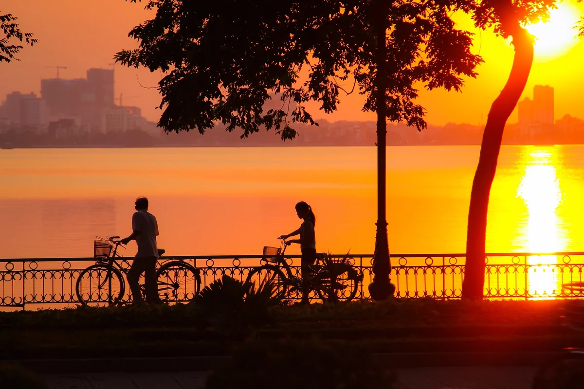 Two people on bikes near a lake as the sun sets