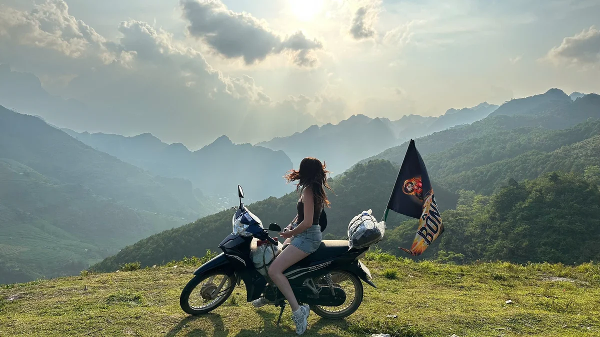 Woman poses on a motorbike with mountains and clouds behind