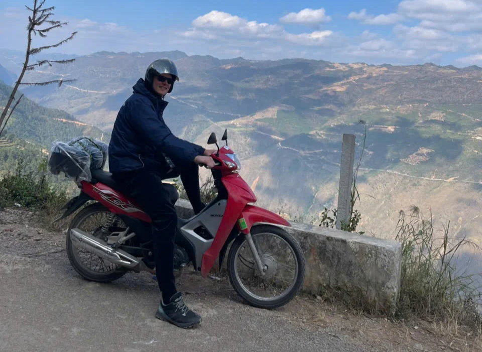 Man sitting on a motorbike with blue skies and mountains behind
