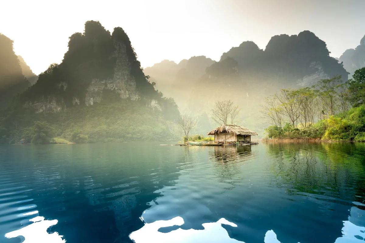 a house boat floating on top of a lake with mountains behind