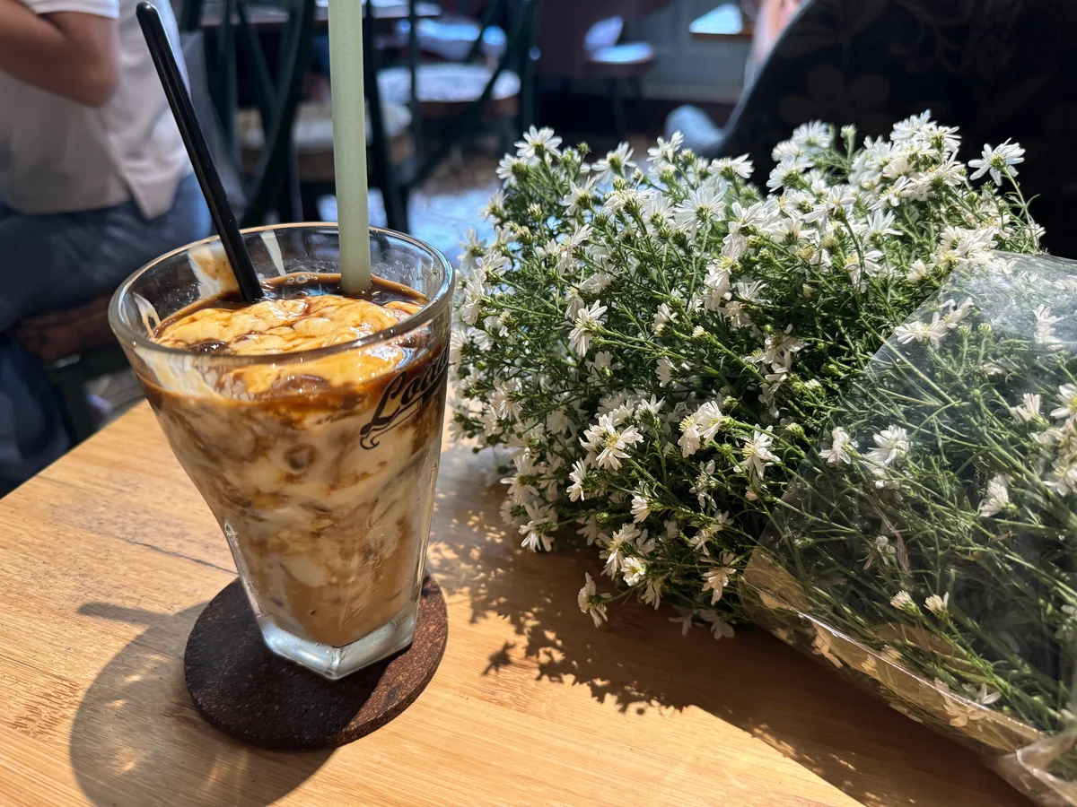 A coffee on a table next to a bunch of flowers at a cafe in Vietnam