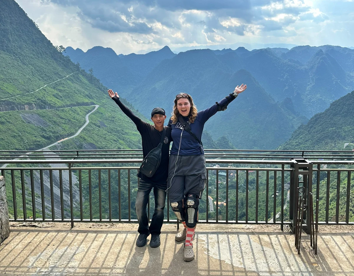 A tour guide and his guest pose with the mountains behind