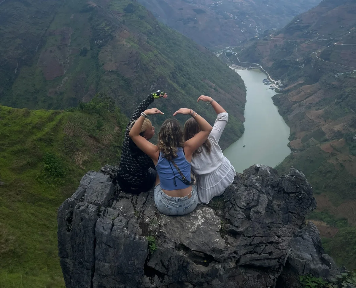 Three people create a heart shape with the Nho Que river beyond