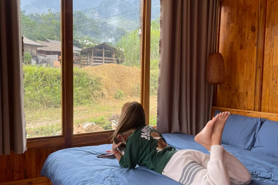 Girl lies on a bed looking out a window of Bong Hostel Ha Giang Loop accommodations