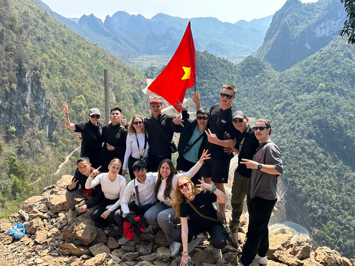 A group of people pose for a photo with peace signs, scenery behind is beautiful