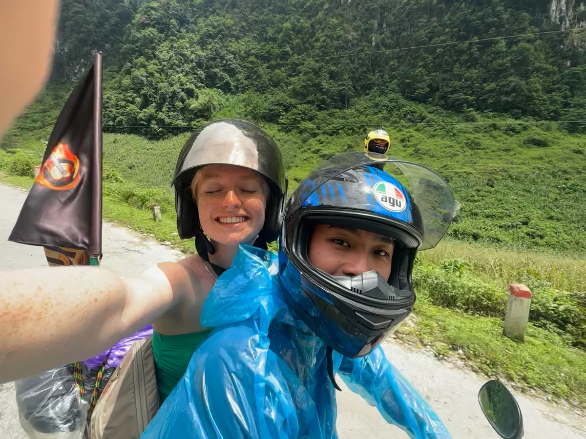 Two people smiling at the camera while riding a motorbike