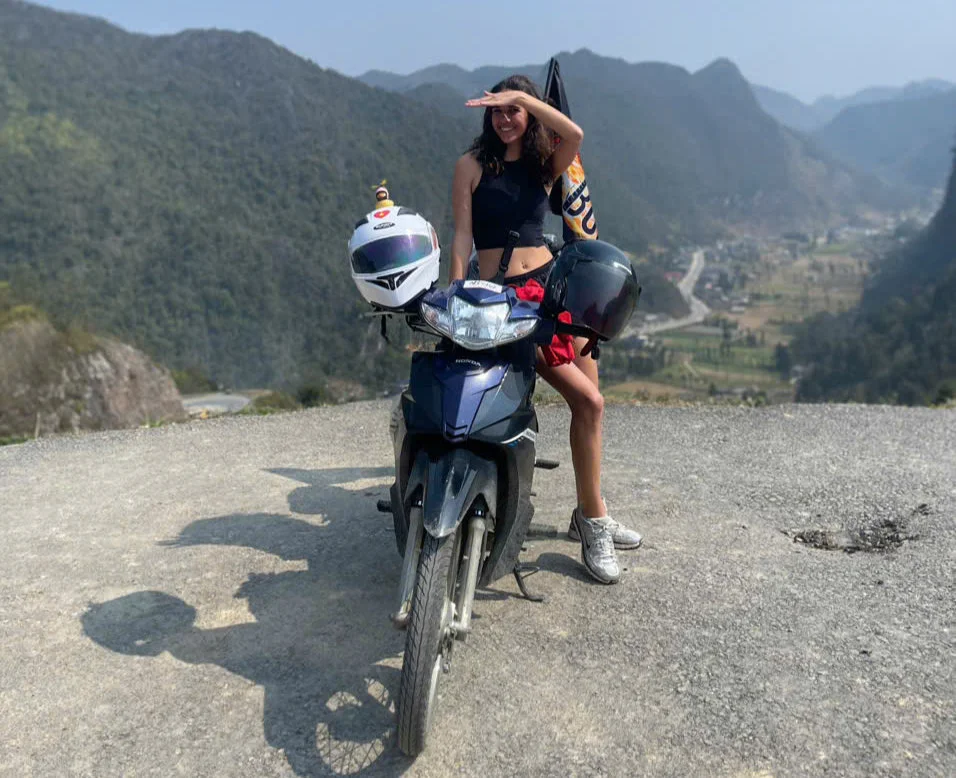 Girl poses by a motorbike against a mountain backdrop in Ha Giang