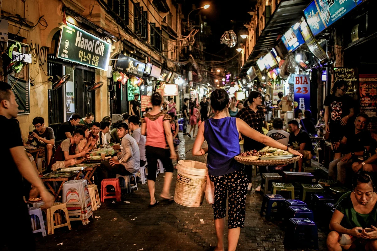 Two women walking through a street lined with tables and men drinking