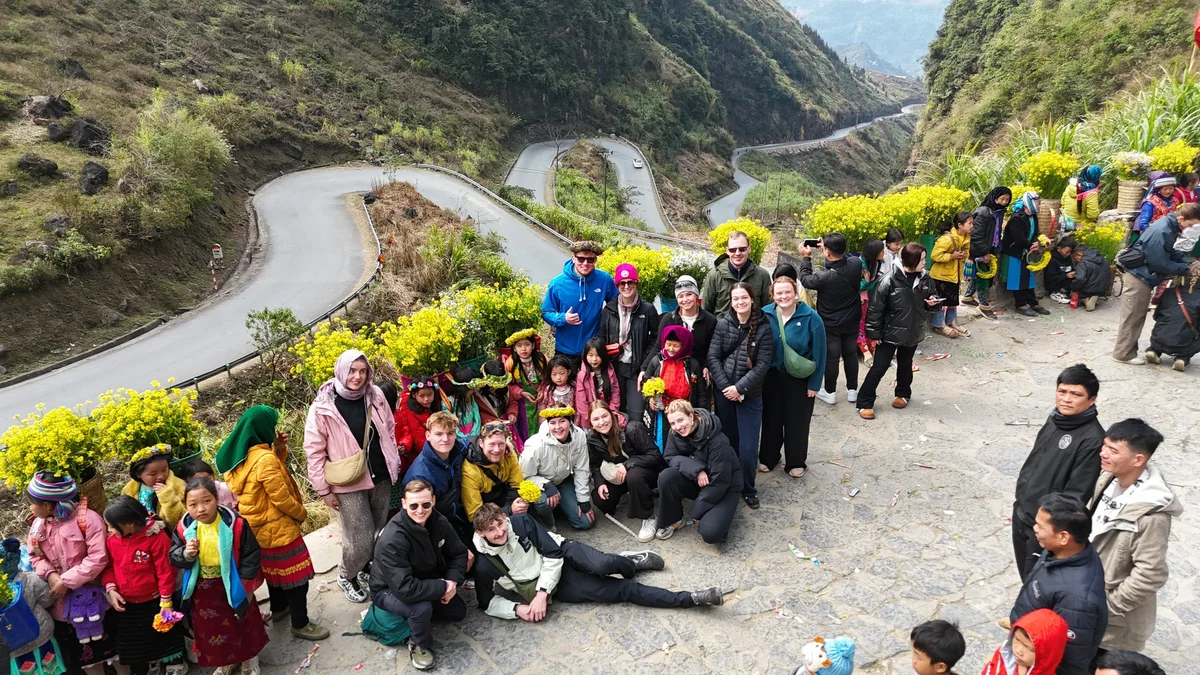 Large group of people smile at the camera with the Tham Ma Pass in the background