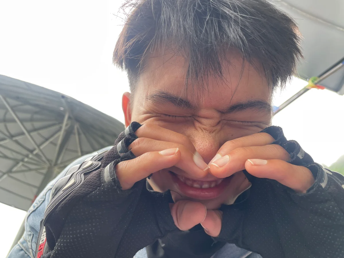 Young person wearing fingerless gloves playfully squints and grins under a large umbrella. The mood is cheerful and lighthearted.
